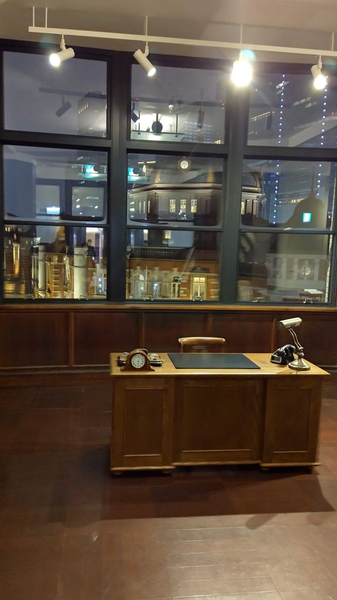 窓辺に置かれた木の机と木の床の部屋。窓の外にライトアップされた駅舎が見える